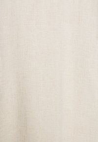 Naturalny materiał lniany w kolorze off-white, z subtelną fakturą i delikatnymi, tkanymi włóknami, co nadaje mu miękki, lekki wygląd.