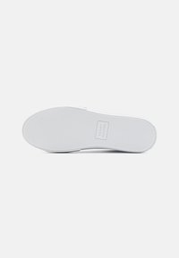 White rubber shoe sole with a textured surface and rounded toe. Logo "Tommy Hilfiger" visible in the center. Smooth edge and minimalist design.