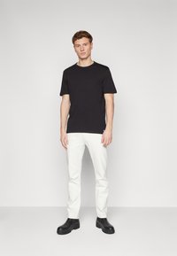 T-shirt nera a maniche corte, abbinata a pantaloni bianchi e stivali neri con tacco. Tessuto morbido con scollatura rotonda e design aderente.