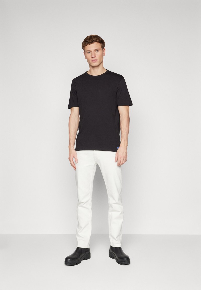 T-shirt nera a maniche corte, abbinata a pantaloni bianchi e stivali neri con tacco. Tessuto morbido con scollatura rotonda e design aderente.