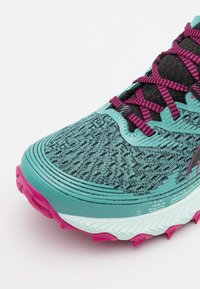 Chaussure de course bleu sarcelle et noire avec des lacets et une semelle rose, tige en tissu texturé, et une semelle intercalaire épaisse et amortissante avec une semelle extérieure crantée.