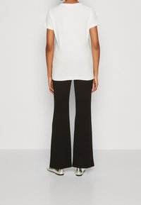 Camiseta blanca de manga corta, acompañada de pantalones negros de campana. Presenta zapatos metálicos brillantes, creando un contraste con el atuendo.