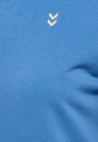 Fond en tissu bleu avec deux petites flèches blanches en chevron positionnées près du centre en haut, texture légèrement en relief visible.