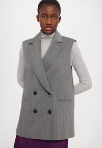 Blazer fără mâneci, gri cu dungi subțiri, cu un design cu două rânduri de butoane, având rever cu colțuri și buzunare frontale, asortat cu un pulover cu gât închis, de culoare gri deschis.