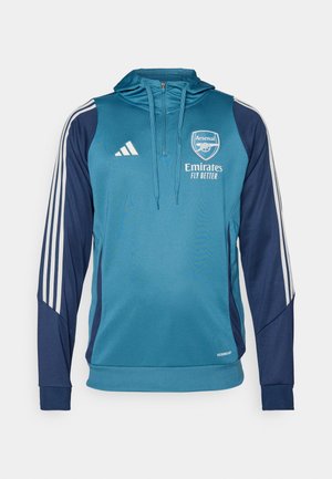 Teal og marineblå hettegenser med hvite Adidas-striper, logo og teksten "Emirates Fly Better". Myk stoff, atletisk passform og glidelås.
