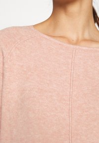 Maglione a maglia rosa chiaro con scollo rotondo, texture a coste e motivo orizzontale sottile. Presenta maniche a raglan e una cucitura centrale.