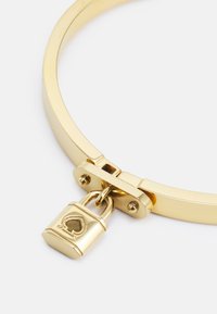 Arany bangle karkötő sima felszínnel és szívmotívumos zárkájjal. A csat és a zsanér integrált a biztonságos zárás érdekében.