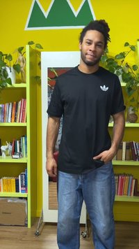 T-shirt preta de manga curta com logótipo branco, combinada com jeans azul claro desgastados, contra um fundo amarelo vibrante com prateleiras.