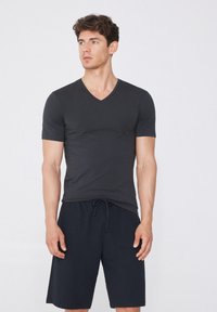 Camiseta negra de cuello en V hecha de una tela suave, combinada con pantalones cortos oscuros. Presenta mangas cortas y un diseño ajustado. Aspecto simple y limpio.