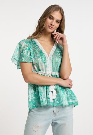 Grøn mønstret bluse med korte, gennemsigtige ærmer, V-hals, blondekant og elastisk talje med hvide kvaster. Bæres med lyse jeans.