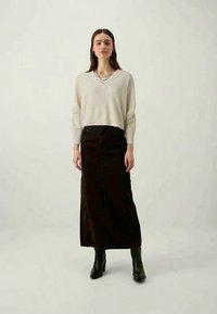 Krems krūšu izgriezuma džemperis, kas saskaņots ar melnu maxi svārku. Apģērbu papildina melni potīšu zābaki un kārtotās sudraba kaklarotas.