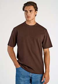 Brun t-shirt med kort ärm i mjukt tyg, med rund hals och avslappnad passform. Matcher med blålila denimjeans.