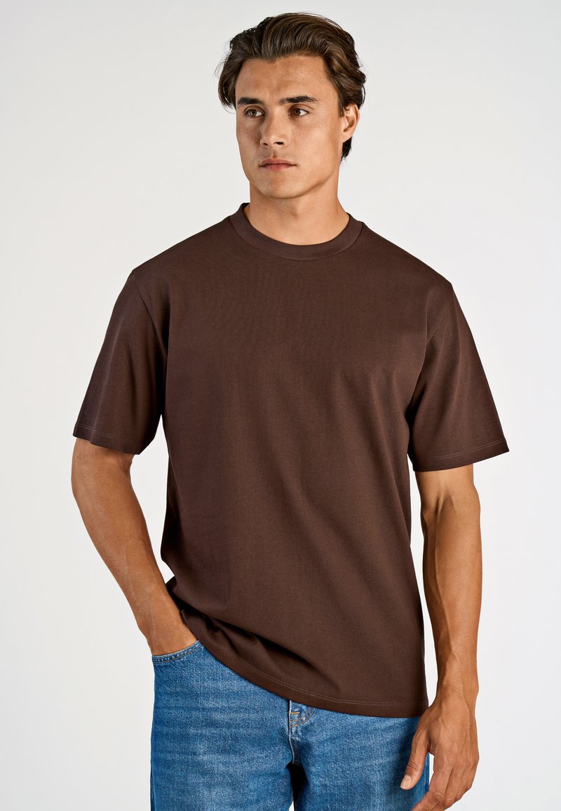 Brun t-shirt med kort ärm i mjukt tyg, med rund hals och avslappnad passform. Matcher med blålila denimjeans.