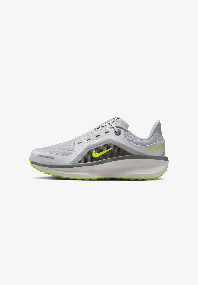 Scarpa sportiva grigia con tomaia testurizzata, accenti verde neon, suola ammortizzata e design leggero. Presenta un logo visibile e dettagli.