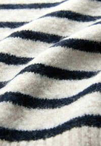 Uldtrøjestof har skiftevis marineblå og creme striber, med en blød, tekstureret overflade og en let glans fra fibrene.