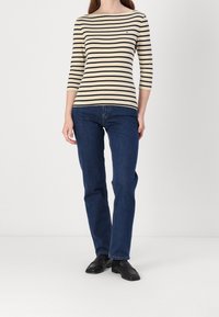 Pruhované tričko s dlouhým rukávem v krémové a námořnické modři, spárované s tmavě modrými džínami. Tričko má široký výstřih a rukávy po lokty.