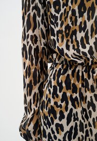 Tkanina s leopardjim vzorom ima rjave, črne in peščene pike. Oblačilo ima zategnjen pas in dolge rokave z gladko teksturo.
