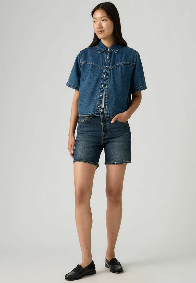 Veste-chemise en denim à manches courtes avec un col à revers, associée à un short en denim foncé. Les deux présentent une finition classique et un design simple.