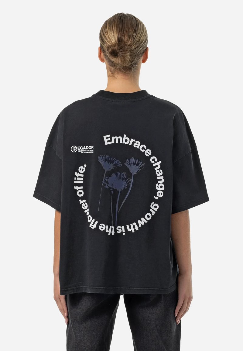 Svart oversized t-skjorte med blomstermotiv og tekst på baksiden. Laget av bomull med en avslappet passform og kortermede.