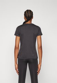 Fekete, rövid ujjú sportpóló, testhezálló kialakítással, kerek nyakkivágással és sima textúrával, fekete leggings-szel párosítva.