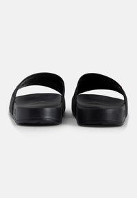 Musta sandaalit litteällä muotoilulla, joissa on leveät hihnat ja teksturoitu pohja. Materiaali vaikuttaa synteettiseltä, sileillä pinnoilla ja pyöristetyillä reunoilla.