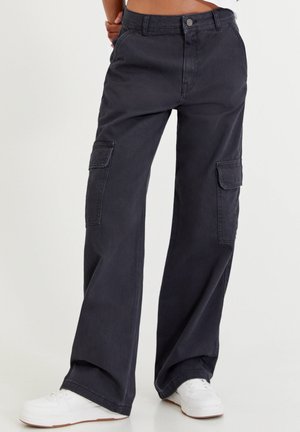 Pantalons cargo gris foncé en coton, dotés de jambes larges, de poches latérales et d'une fermeture à bouton. Associés à des baskets blanches.