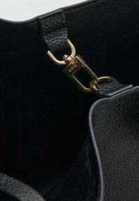 Close-up of a black textured leather strap attached to a gold metal clasp inside a black bag interior.
