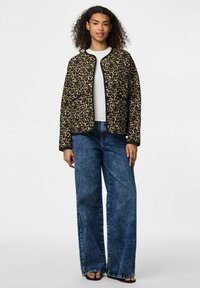 Leopardmönstrad jacka med svart trim och tryckknappsstängning; kombinerad med vida denimbukser. Texturen verkar mjuk och designen är avslappnad.