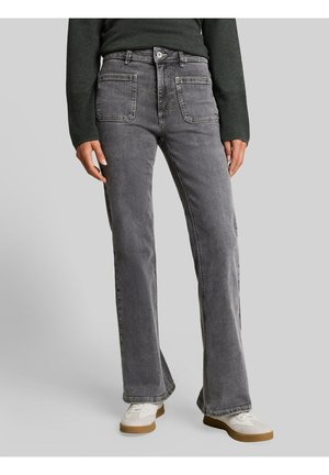 Person trägt hoch taillierte graue Jeans mit Vordertaschen, ein dunkles Langarmoberteil und weiße Sneaker mit braunen Sohlen.