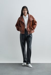 Brūna ādas īsa jaka ar platu apkakli, rāvējslēdzēja priekšpusi un sprādzēm. Kombinēta ar melnām plaša piegriezuma biksēm un baltām sporta kurpēm.