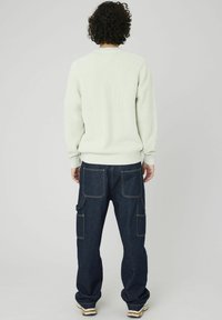 Pull en tricot côtelé vert clair avec un col rond, associé à un pantalon cargo en denim bleu foncé doté de plusieurs poches et de coutures contrastées.