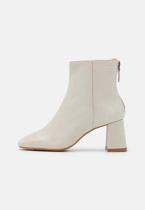 Bottine beige texturée avec talon épais, fermeture éclair arrière, bout pointu et semelle lisse sur fond blanc.