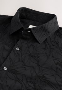 Schwarzes Hemd mit einem bestickten Blumenmuster, Knopfverschluss am Kragen und strukturiertem Stoff.