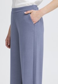 Pantalon de sport bleu clair en tissu lisse, doté d'une taille élastique et de poches latérales, avec un design épuré à jambes larges.