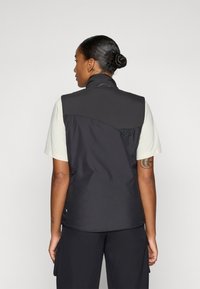 Gilet nero con colletto alto, tessuto leggero e texture liscia. Presenta un pannello posteriore a contrasto e dettagli in rete.