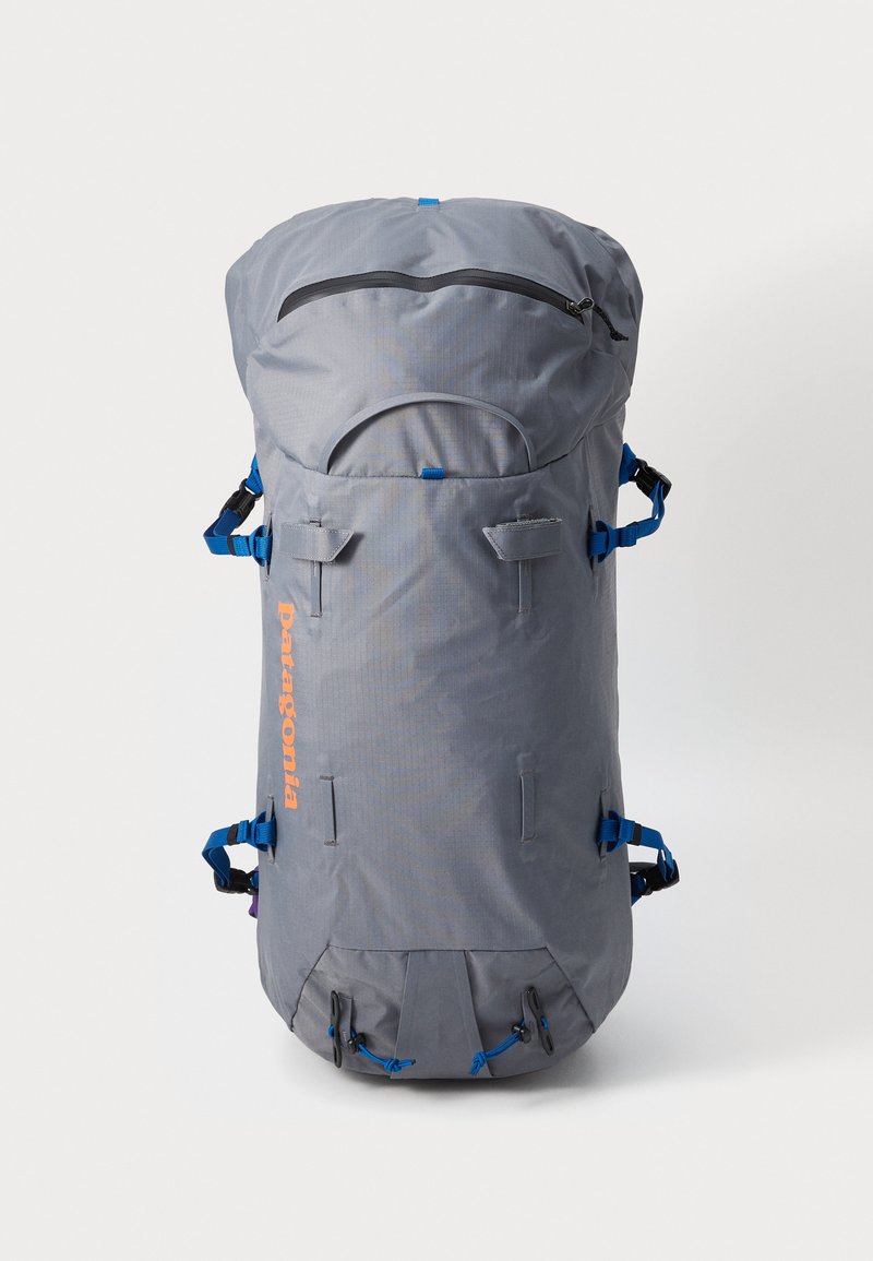 Gray backpack with a rounded top, blue straps, and an orange logo. Features a zip pocket and multiple straps for attachment. Durable fabric.