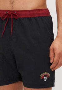 Calções de banho pretos com uma cintura elástica vermelha e cordão. Apresenta um colorido logótipo bordado "Santa Cruz" com um sombrero e uma caveira.
