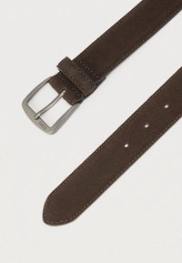 Καφέ ζώνη από σουέτ με πόρπη από βουρτσισμένο μέταλλο, διαθέτοντας αντίθετο ράψιμο και πολλαπλές τρύπες ρύθμισης κατά μήκος του ιμάντα.