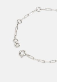 Collana in argento composta da anelli metallici, con forme ovali e circolari, dotata di chiusura a moschettone e un piccolo cartellino attaccato.
