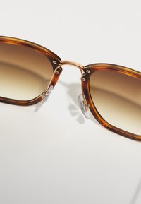 Ochelari de soare tortoiseshell maroniu cu lentile gradient, accente din metal și pernuțe nazale transparente. Formă pătrată rotunjită, finisaj neted.