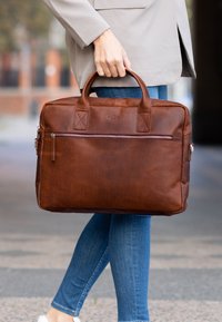 Valigia in pelle marrone con due manici superiori, una tasca frontale con zip e dettagli testurizzati. Design robusto, adatto per uso professionale.