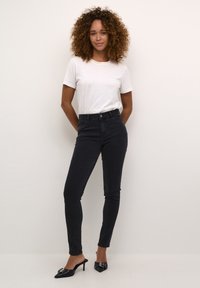 Jeans noirs taille haute à coupe slim, associés à un t-shirt blanc et des mules noires à talons hauts avec une boucle décorative.