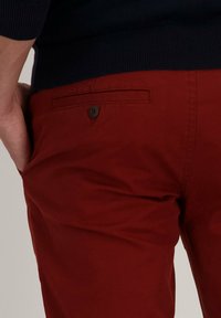 Rode katoenen chinos met een gladde textuur, voorzien van een achterzak met een bruine knoopaccent en een aansluitende tailleband.