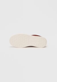 Suole delle scarpe in gomma beige con motivo triangolare e logo "GUESS", viste dal basso su uno sfondo bianco.