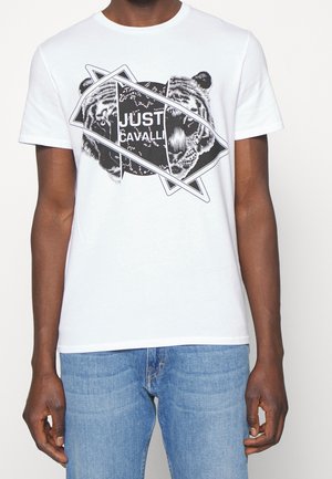 Biała koszulka bawełniana z czarnym graficznym wzorem z twarzami tygrysa i akcentami geometrycznymi, z napisem "JUST CAVALLI" wkomponowanym w projekt.