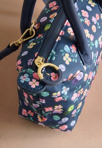 Sac à main floral en tissu bleu marine orné de fleurs multicolores, ferrures dorées et poignée en cuir bleu foncé. Fermeture éclair incluse.