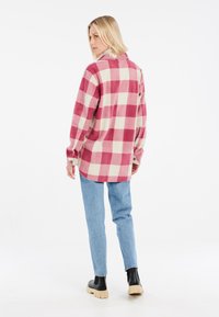 Chemise en flanelle à carreaux rouge et crème avec col, manches longues et poignets boutonnés, assortie à un jean bleu clair et des bottes à plateforme noires.