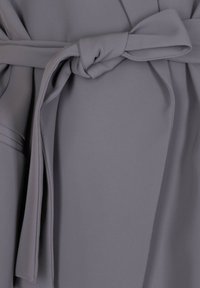 Indumento in tessuto grigio con cintura a nodo, caratterizzato da una texture morbida e liscia e da un design fluido, evidenziato da pieghe e un dettaglio a fiocco annodato.