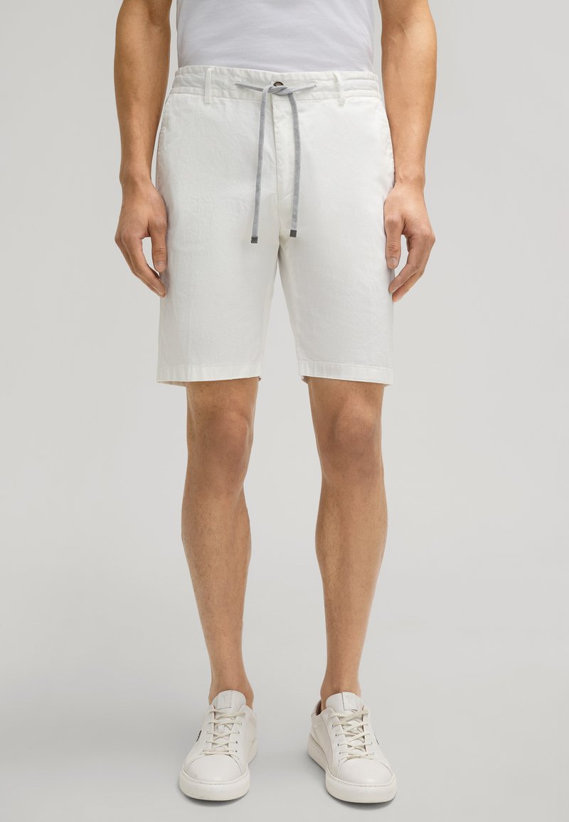 White cotton shorts with a drawstring waist and rolled hems, featuring a textured finish. Paired with white sneakers for a casual look.