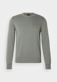 Vaalea harmaa pitkähihainen pyöreäkauluksinen neule, jossa on ribbireunat hihansuissa ja helmassa. Vasemmassa rinnassa pieni neliölogo-merkki.